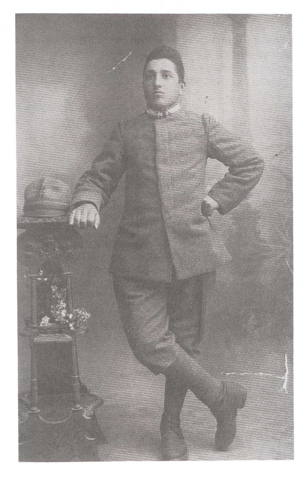 Très vieille image d’un jeune garçon debout avec ses jambes croisées et sa main repose sur une étagère.