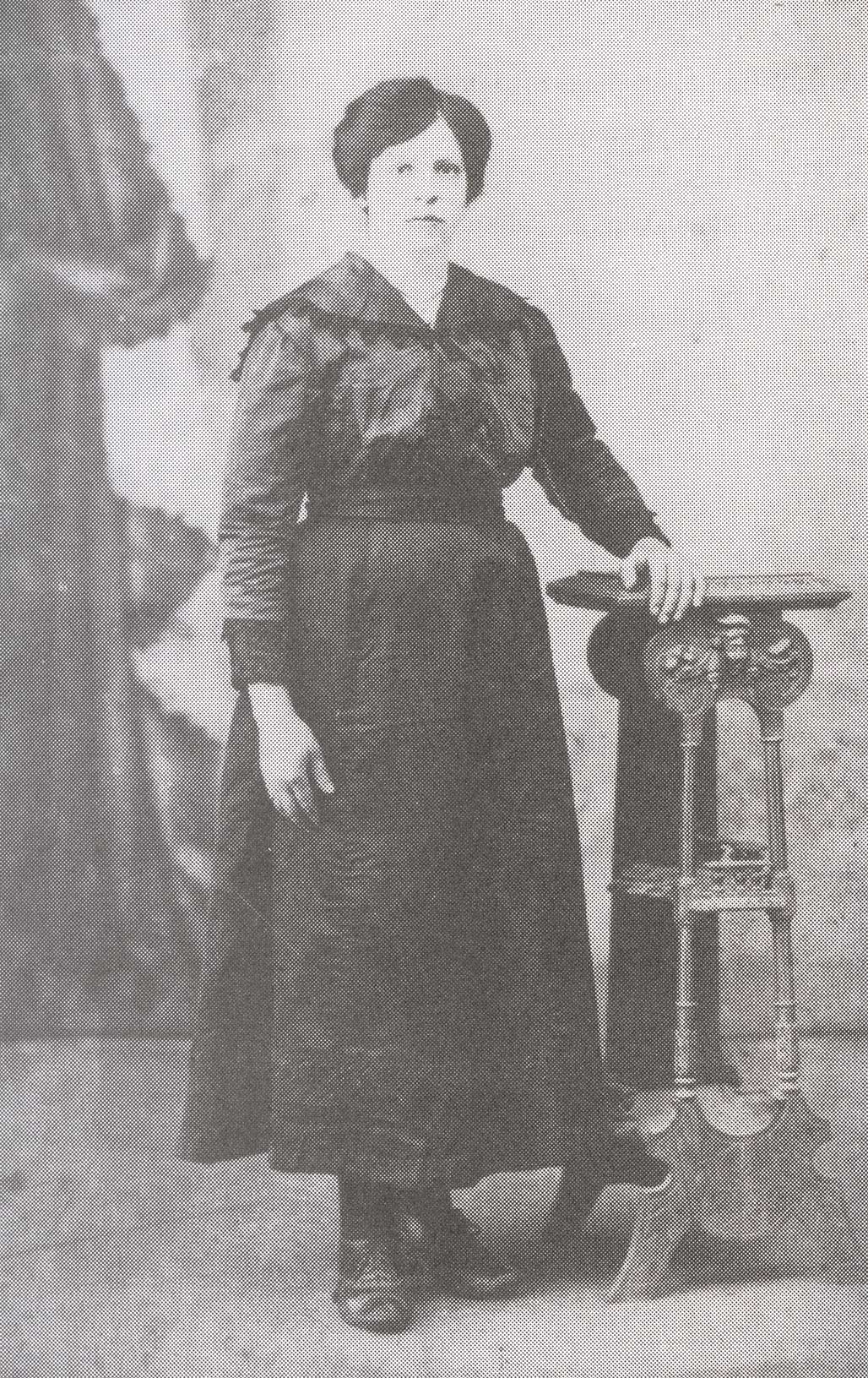 Vieille image d’une femme en robe noire, debout la main sur une étagère.