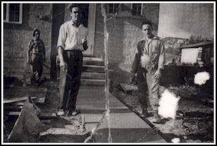 Vieille photo craquelée montrant trois hommes travaillant sur le ciment marcher à l’extérieur de la maison.