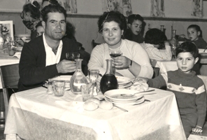 Jeune homme, femme et enfant assis à la table à dîner chargée d’assiettes et de verres.