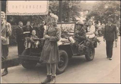 Un petit défilé avec une jeep militaire suivi de deux femmes tenant une bannière.