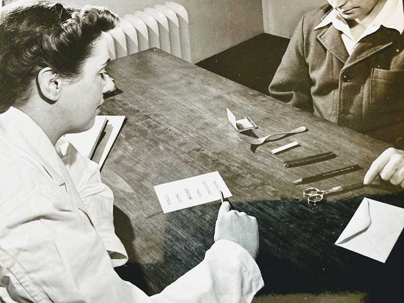 Deux jeunes femmes sont assises à une table; il y a des ciseaux et du papier sur la table.