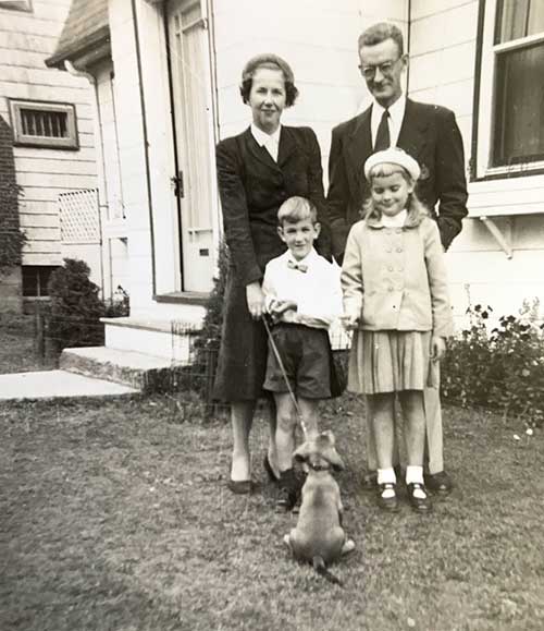 Couple avec deux enfants et un chien debout devant leur maison pour une photo.
