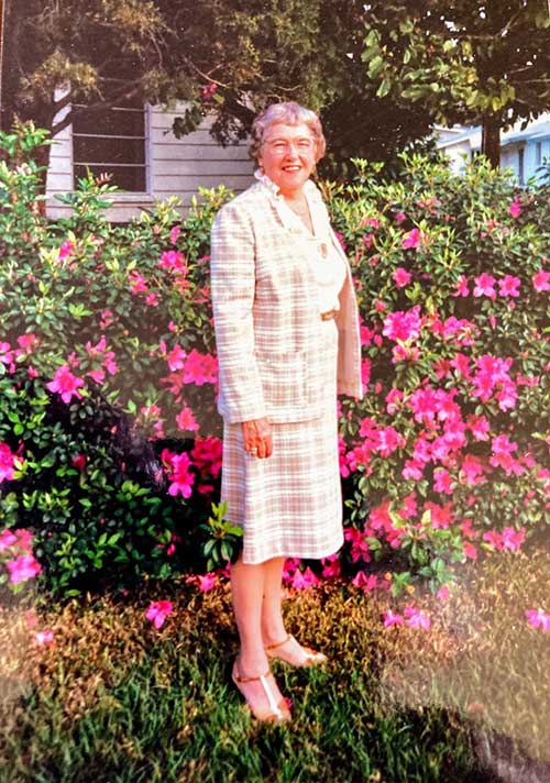 Une jeune femme bien habillée se tient devant un jardin fleuri.