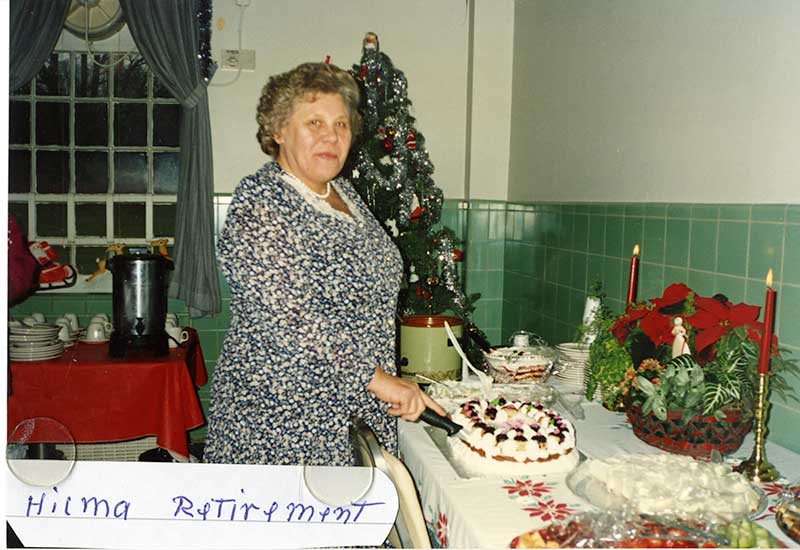 Femme debout devant une table chargée de décoration de Noël et de nourriture.