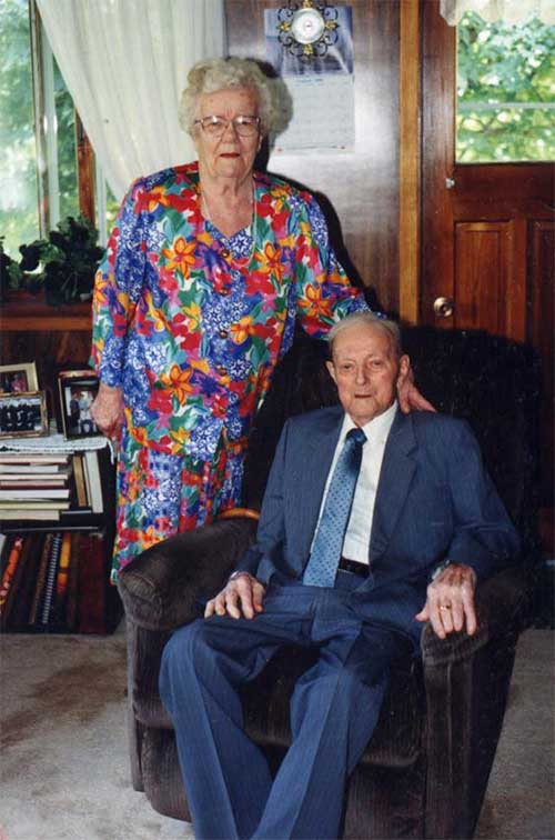 Un homme âgé est assis et une femme âgée est debout à côté de lui.