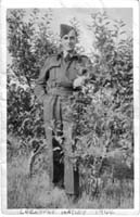 Jeune homme en uniforme de marin, debout devant de petits arbres.