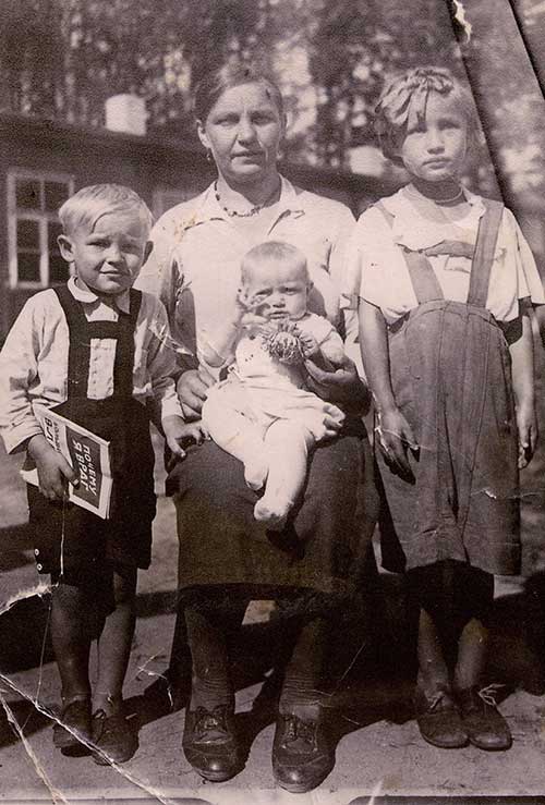 Photo archivée d’une jeune femme assise avec un bébé sur ses genoux et de deux jeunes enfants debout à côté d’elle.