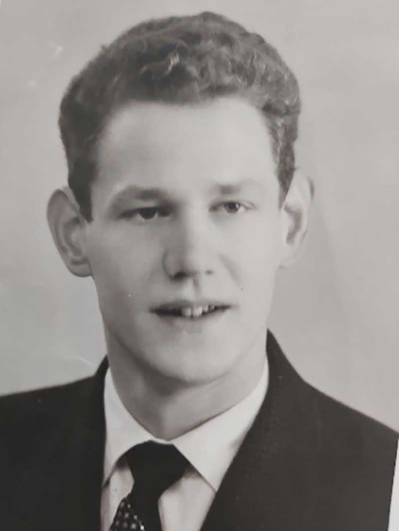 Portrait d’un jeune homme, habillé en costume et cravate, sourit.