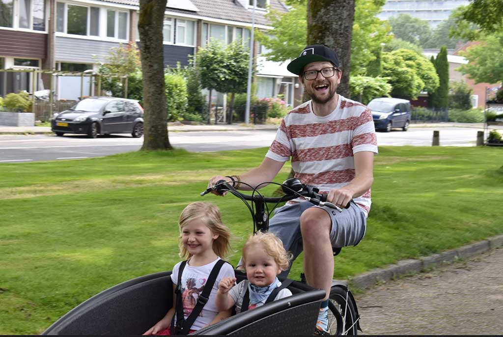 Un jeune homme fait du vélo avec deux petits enfants dans le baquet.