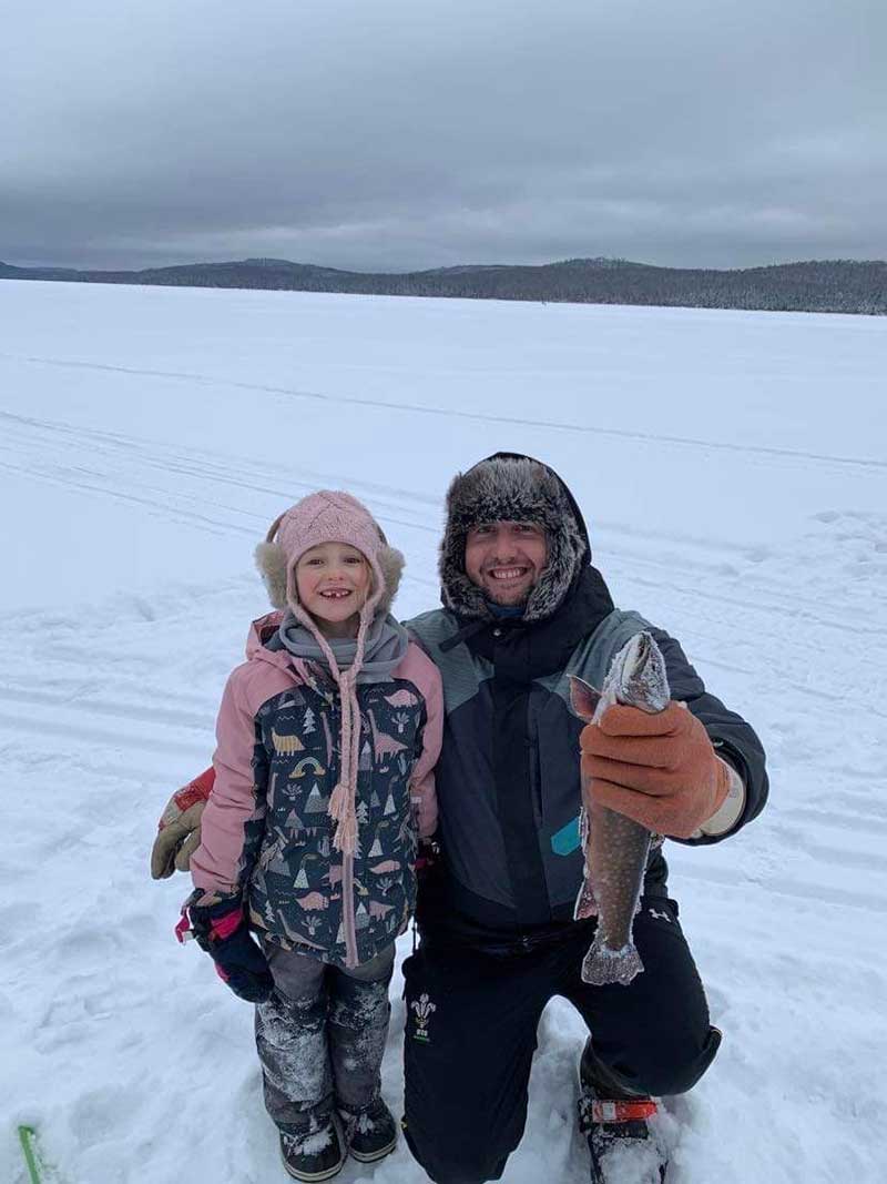 Petite fille et jeune homme sur un lac gelé, l’homme tient un gros poisson.