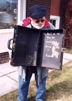 Homme barbu portant un béret bleu, affichant à l’intérieur une vieille valise usée.