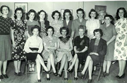 Photographie de groupe de cinq jeunes femmes assises et plusieurs autres debout derrière elles.
