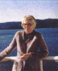 Photo en couleur d’une femme plus âgée, avec de l’eau bleue en arrière-plan.