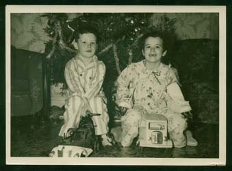 Sandra et son frère Ken enfants, en pyjama, assis devant un arbre de Noël.