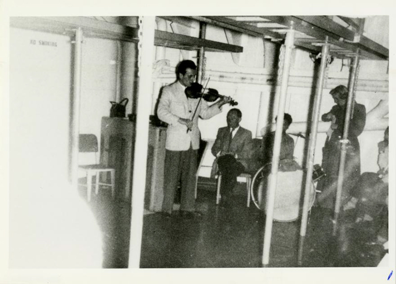 Vieille image en noir et blanc de l’homme jouant du violon sur un navire pendant que d’autres personnes l’écoutent.