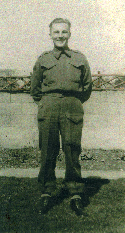 Bel homme portant l’uniforme militaire debout devant le mur avec le visage souriant.