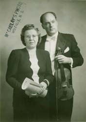Janis tenant un violon et un archet, et Felicita debout à ses côtés.