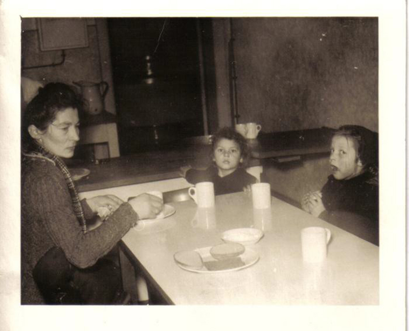 Une jeune femme avec deux enfants assis autour de la table, qui a trois tasses et du pain sur elle.