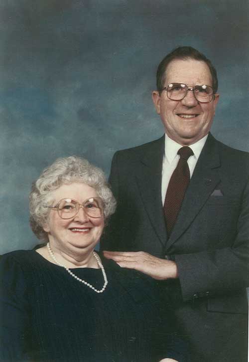 Portrait en couleur d’un couple. La femme est assise et porte un collier de perles et l’homme est debout à ses côtés.