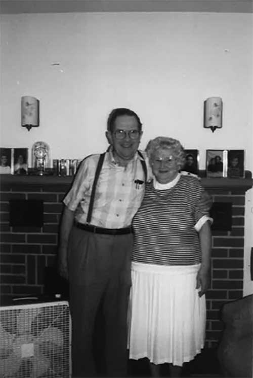 Un homme et une femme debout devant un foyer. Il y a un petit ventilateur près d’eux.