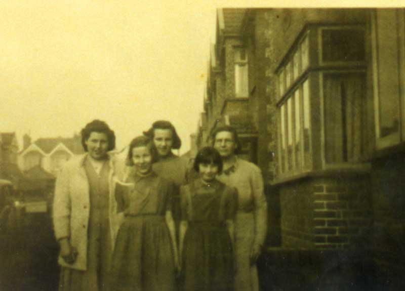 Cinq dames jeunes et d’âge moyen, debout devant la maison pour une photo.