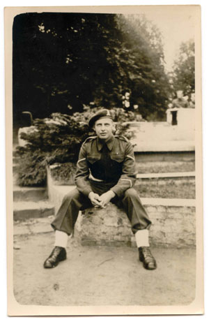 Le jeune Hugh en tenue militaire, assis sur un mur de pierres.