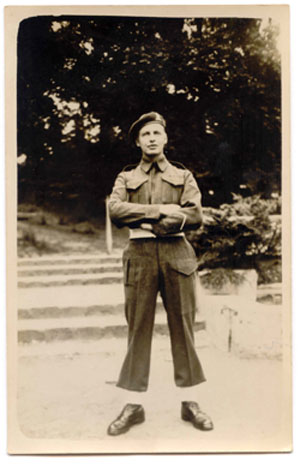 Le jeune Hugh debout les bras croisés, portant une tenue militaire. 