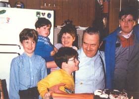 Leland plus âgé, assis dans la cuisine, entouré par cinq petits-enfants. 