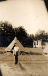 Photographie décolorée du jeune William debout dans un champ, des tentes à l’arrière-plan.