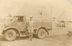 Jeune homme en tenue militaire debout devant un camion de transport.
