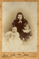 Portrait décoloré d’un bébé garçon en blanc et de deux petites filles en robe sombre.