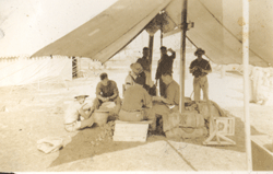 Photographie décolorée montrant plusieurs jeunes hommes sous une tente sur un terrain militaire.