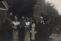 Jeunes mariés et cortège nuptial devant un immeuble en briques.