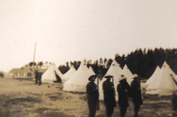 Quatre jeunes hommes en tenue militaire, au garde-à-vous devant des tentes.