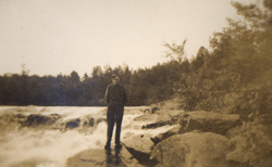 Jeune homme en tenue militaire, debout sur un rocher à proximité d’une rivière.