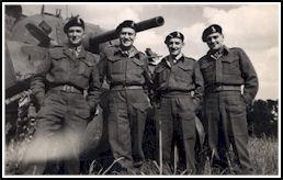 Quatre jeunes hommes en tenue militaire et béret, debout devant un tank de l’armée. 