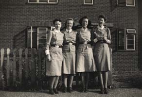 Quatre jeunes femmes en uniforme d’infirmière de l’armée, debout devant un immeuble.