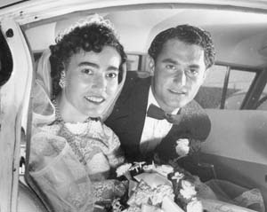 Jeunes époux assis à l’arrière d’une voiture, le jour de leur mariage. 