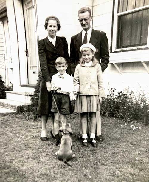 Un jeune homme et une jeune femme avec deux enfants et un chien se tiennent devant une maison.