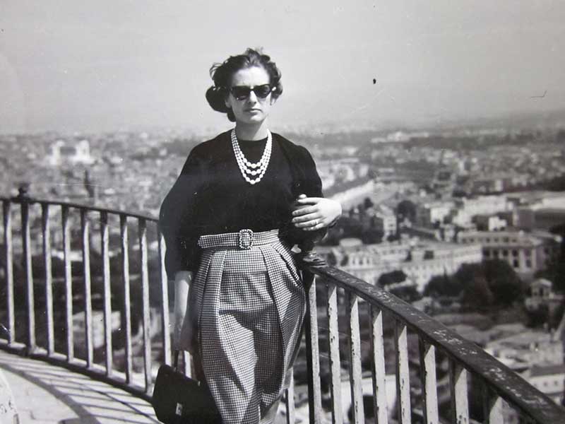 Une jeune femme bien habillée, appuyée contre une balustrade surplombant une belle ville.