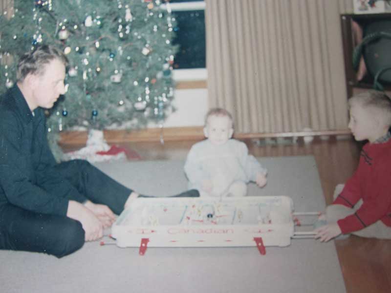 Un homme et un jeune enfant assis devant un arbre de Noël. Ils regardent des jouets.