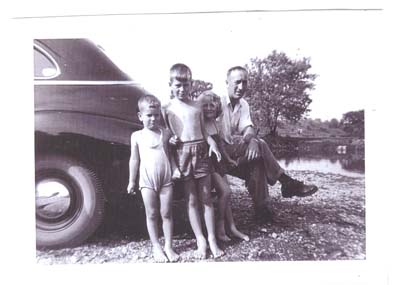 Le jeune George et trois enfants assis sur le pare-choc arrière d’une voiture. 