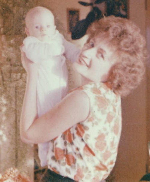 Une jeune femme aux cheveux roux tient un beau bébé vêtu de blanc.