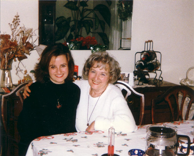 Deux femmes assises à la table à dîner se lient les bras et sourient pour la caméra.