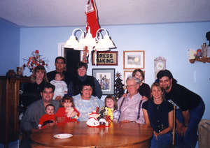 Photographie couleur de Mels plus âgé, entouré par les plus jeunes générations des membres de la famille. 
