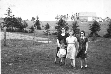 Trois jeunes femmes avec une petite fille, debout dans un champ ouvert.