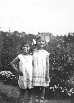 Deux jeunes filles dans un jardin, portant des robes d’été blanches et des rubans dans les cheveux.