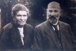 Femme et homme barbu, tous deux vêtus de couleurs foncées.