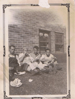 Vieille photo fanée de quatre jeunes hommes assis sur la pelouse à l’extérieur de la maison.